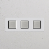 Dreifachrahmen mit 3x Wippschalter auf weißer Wand; lackierbar, poliertes Nickel, schwarz für eleganten Look.
