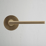 Clayton Fixer Türgriff in antikem Messing mit Niedrigprofilrosette auf heller, strukturierter Wand.