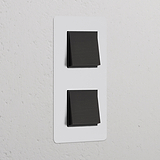 Vertikaler Zweifachrahmen mit 2x Wippschalter, lackierbar in Bronze und Schwarz, montiert an einer weißen Wand.