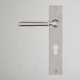 Silberner Digby-Türgriff mit Rückplatte und Schlüsselloch auf weißer Wand, poliertes Nickel-Finish.