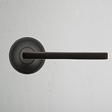 Clayton Fixer Türgriff in Bronze vor einer weißen strukturierten Wand.