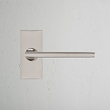 Clayton Fixer Türgriff kurzes Schild aus poliertem Nickel auf strukturierter weißer Wand, mit einem schlanken, modernen Design.