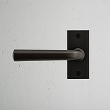 Apsley Fixer Türgriff in Bronze mit kurzem Schild montiert auf einer hellgrauen strukturierten Wand.