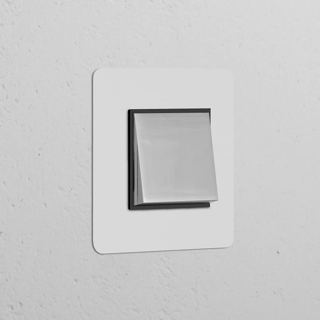 Moderner Einfachrahmen mit Wippschalter, lackierbar, poliertes Nickel und Schwarz, auf weißer Wand.