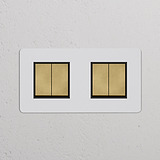 Zweifachrahmen mit 4x Wippschalter in Altmessing und Schwarz, überstreichbar, auf weißer Wand.