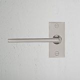 Poliertes Nickel-Türgriff mit kurzem Schild, Clayton Fixer Modell, auf weißer Wand montiert.
