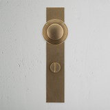 Antiker Türgriff aus Messing mit langer Rückplatte und Knauf, Pappeldesign, auf einer strukturierten weißen Wand.