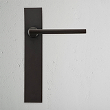 Bronze Clayton gefederter Türgriff mit langem Schild auf einer strukturierten weißen Wand.