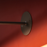 Die bronzefarbene Taylor-Bilderleuchte 220 mm wird elegant an einer leuchtend roten Wand montiert und unterstreicht ihr schlankes Design.