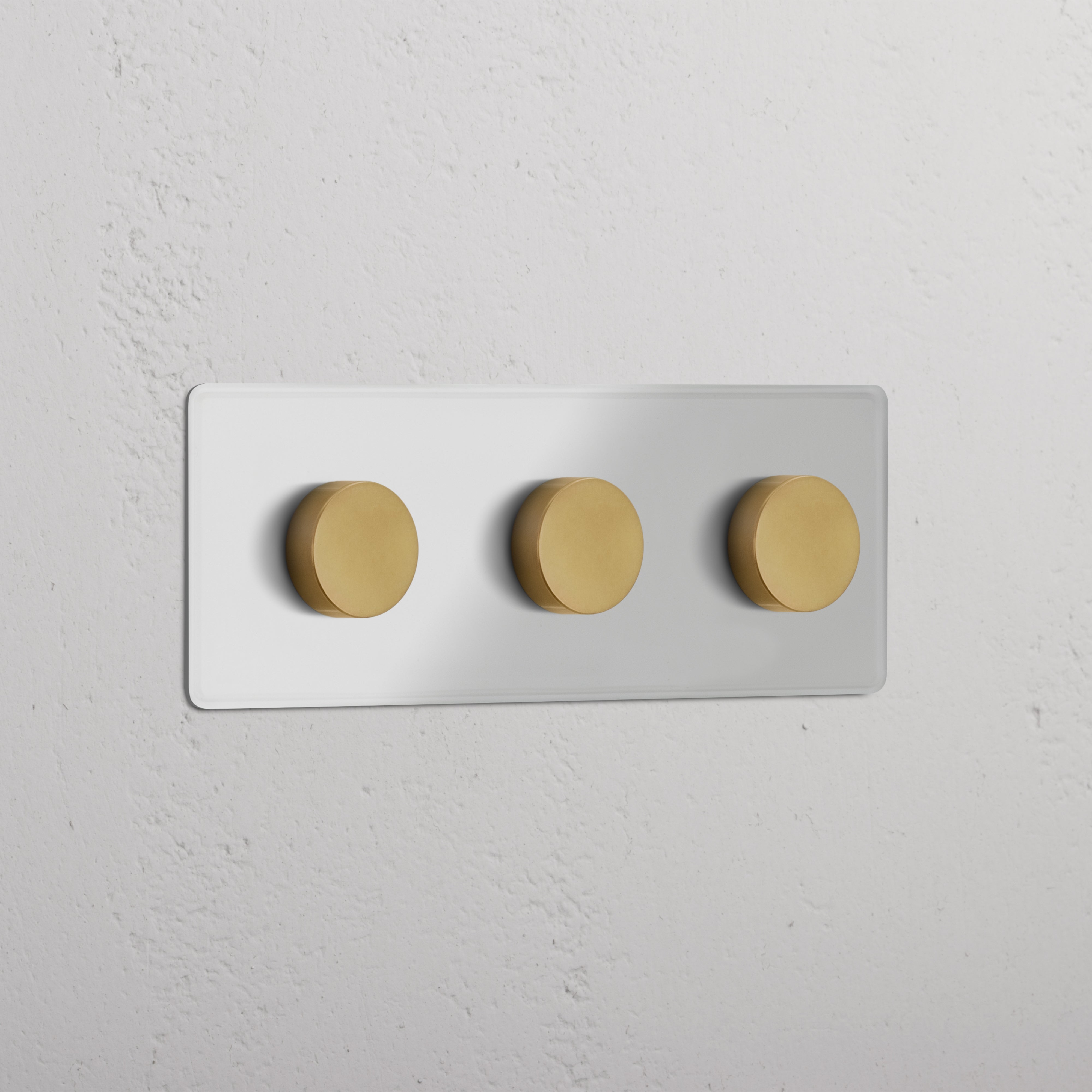 Dreifachrahmen mit 3x Mehrpunkt-Dimmerschalter in Transparent und Antik Messing, montiert an einer weißen Wand.
