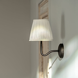 Malvern Medium-Wandleuchte mit alabasterweißem Plisseeschirm und Bronze-Finish an einer hellen Wand.