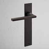 Das gefederte Türgriff-langes Schild von Clayton aus Bronze auf einer hellgrauen Wand unterstreicht sein elegantes und modernes Design.