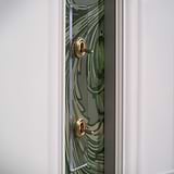 2G Architrave Two Way Toggle Switch in clear antique brass on a decorative green patterned wall.