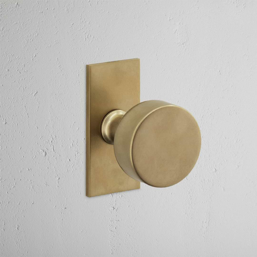 Onslow Short Plate Fixed Door Knob in antique brass, enhancing a textured white wall.