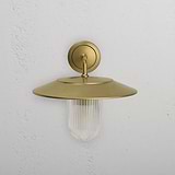 Medium wall light featuring fluted glass and antique brass finish, Kensington Wall Light mounted on white wall.