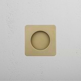 A Regent Recessed Pull in antique brass, square with center hole, on a white textured wall.
