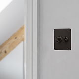 Bronze 2G Two Way Toggle Slimline Switch on white wall near wooden beam.