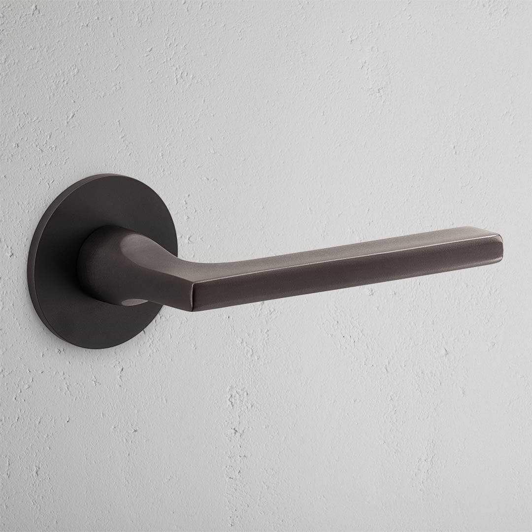 Clayton Flush Rose Unsprung Door Handle in bronze on a textured white wall, perfect for elegant interior doors.