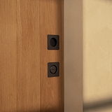 Two black round switches on a wooden wall near a beige surface with an elegant bronze thumbturn.