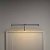 Harrow 400mm Picture Light in bronze elegantly illuminates a plain white panel with minimal design.