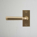 Antique Brass 'Digby Short Plate' Fixed Door Handle on a textured white wall.