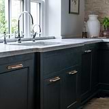 Antique brass Kilburn furniture handle 128mm on green cabinet in modern kitchen with white countertop.