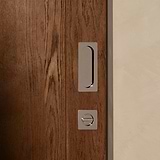Close-up of a wooden sliding door with a polished nickel pull handle and lock against a beige wall.