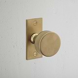 Onslow Short Plate Fixed Door Knob in Antique Brass on rectangular backplate against a white textured wall.