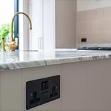 Bronze and black double socket with USB fixed to kitchen sink unit with marble countertop and antique brass tap