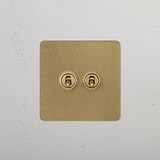 Antique brass 2G retractive toggle switch on a textured white wall for switches & dimmers.