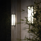 Medium Bank Wall Light Fluted Glass in bronze, mounted on a stucco wall with soft illumination at night.