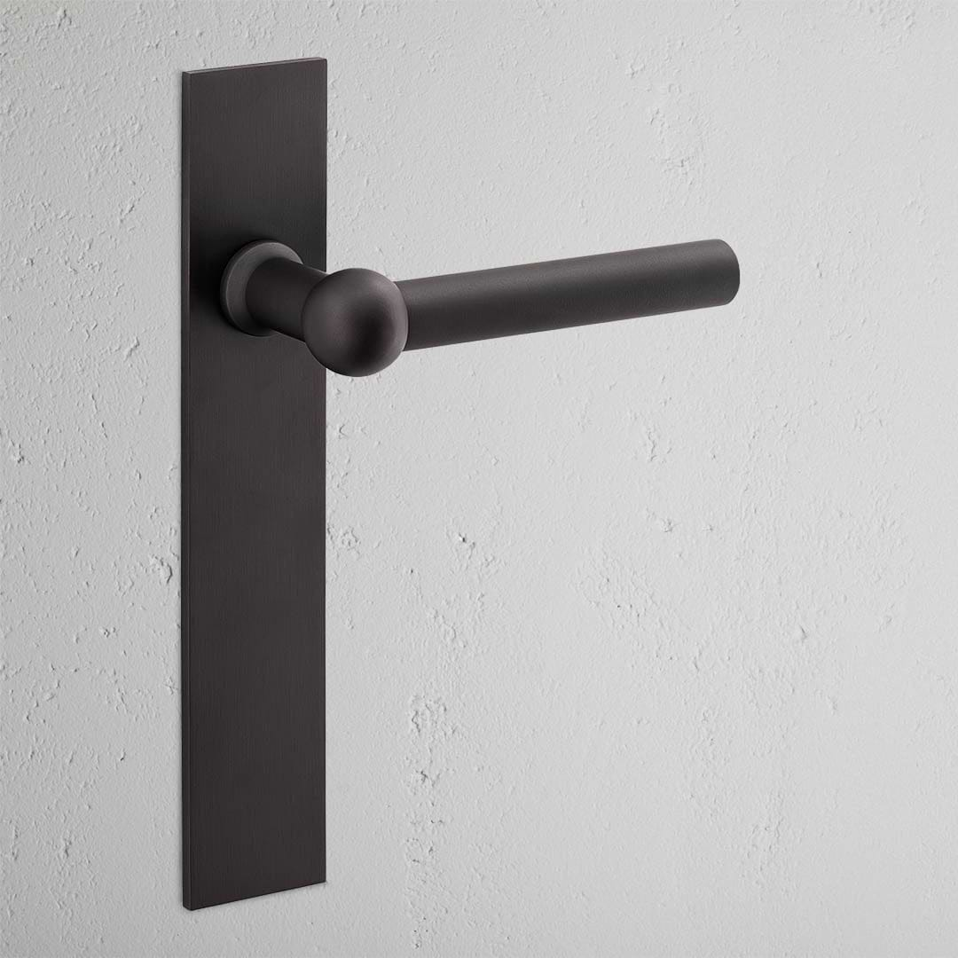 Harper Long Plate Fixed Door Handle in bronze with a rectangular backplate on a light-colored wall.