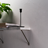 Bronze Brixton Shelf Bracket Supporting a White Marble Stone shelf fixed onto a textured white wall with book, plant and black candle holder.