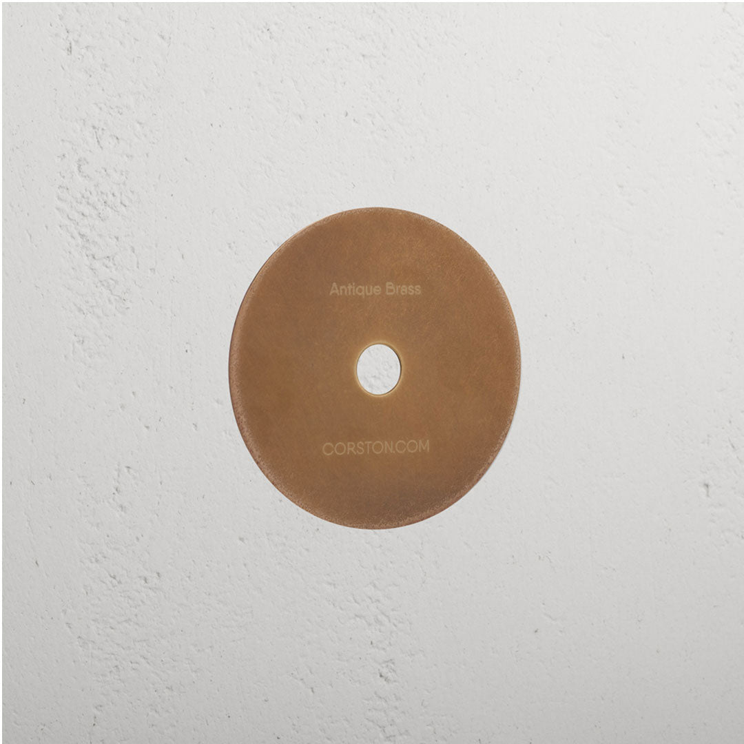 Antique Brass finish sample disc on white textured surface with 'CORSTON.COM' text.