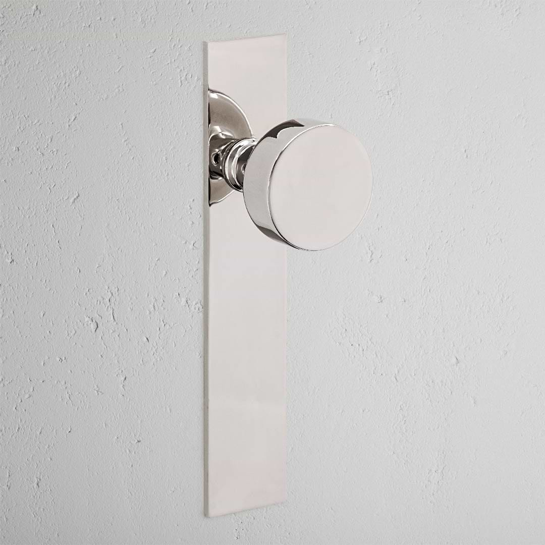 Onslow Long Plate Fixed Door Knob in Polished Nickel, mounted on a white wall; elegant and sleek door handle design.