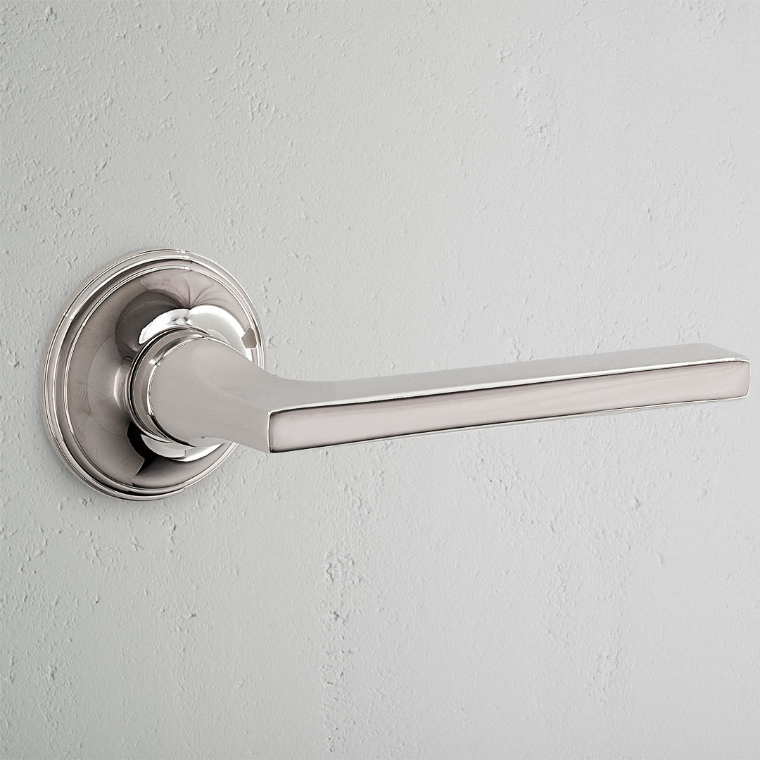 Clayton Fixed Door Handle - Polished Nickel against a light gray wall.