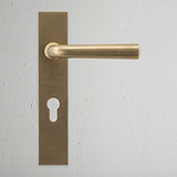 Apsley Long Plate Door Handle & Euro Lock in antique brass on white wall with keyhole beneath.