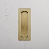 Antique Brass Regent Recessed Pull on a white textured wall.