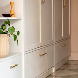 Antique brass Sycamore Furniture Handle 128mm on white cabinets, with decorative items nearby.