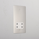 Polished nickel shaver socket with white insert on grey wall. 