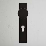Bronze Onslow Long Plate Sprung Door Knob & Euro Lock on a textured white wall with keyhole feature.