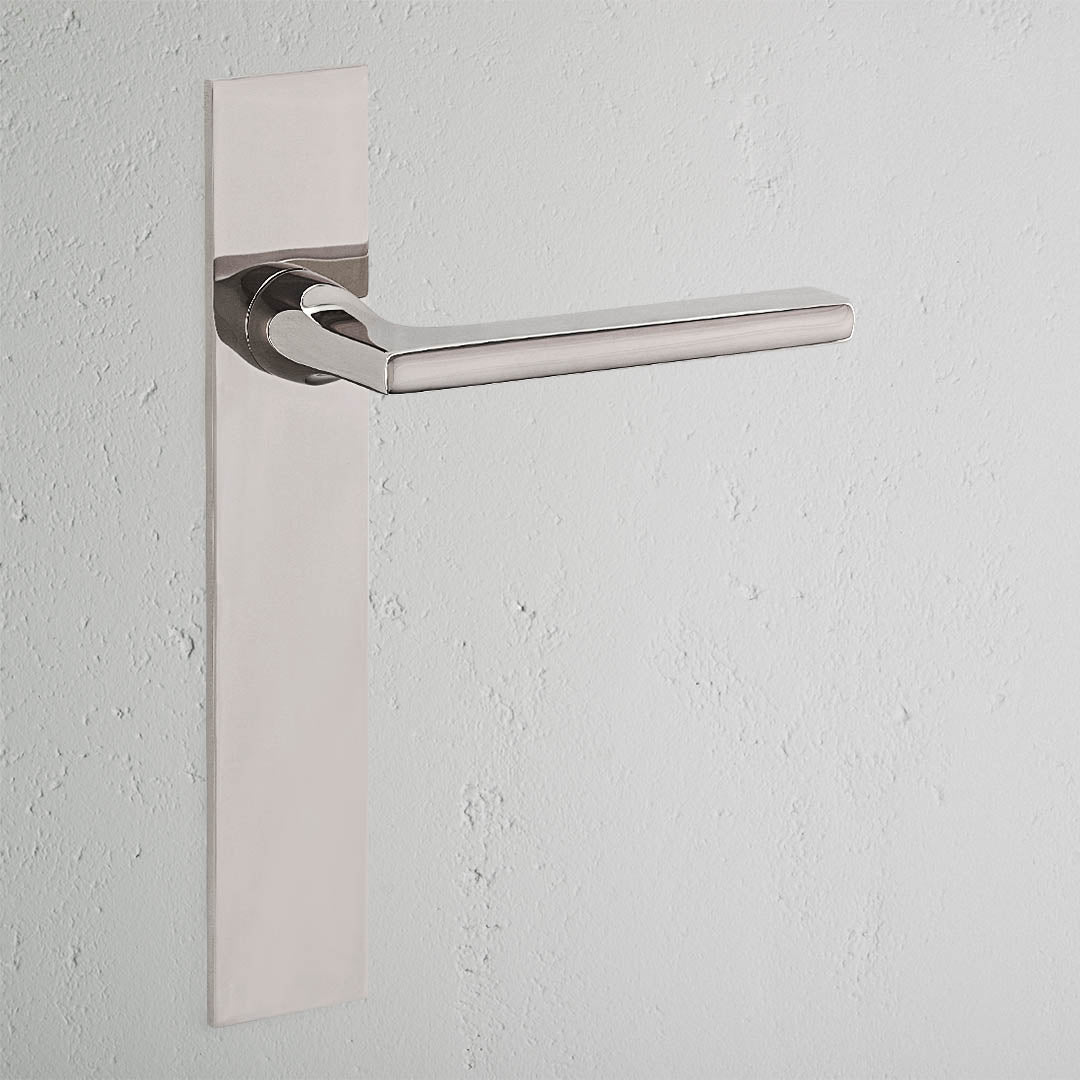 Clayton Long Plate Fixed Door Handle in polished nickel on a white textured wall.