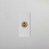 1G Architrave Centre Retractive Toggle Switch, paintable antique brass, on a white textured wall.