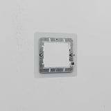 Clear Black 1G 50mm Module Plate with metal bracket, mounted on a white wall, for electrical installation use.