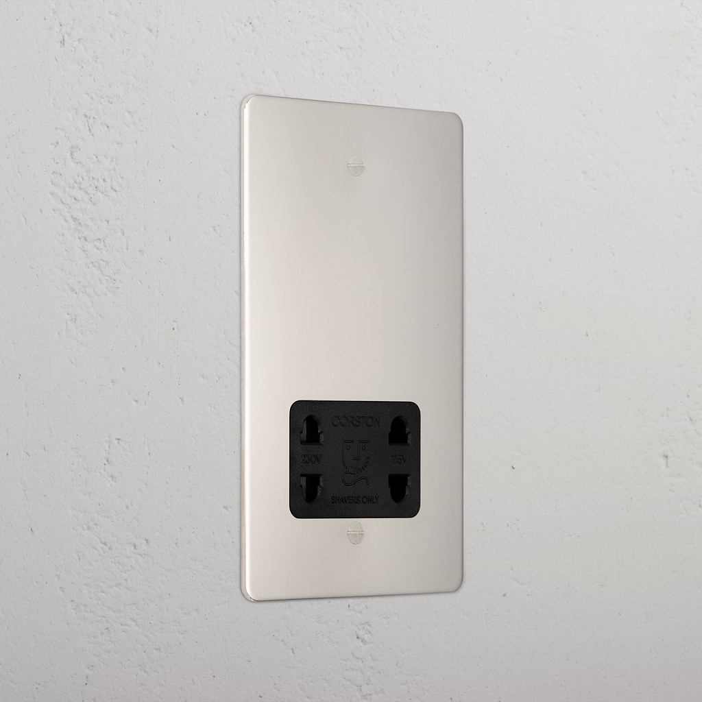 Polished nickel shaver socket with black insert on grey wall. 