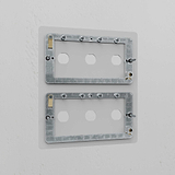Clear 6G switch plate with two metal brackets and six holes for switches, mounted on a white wall.