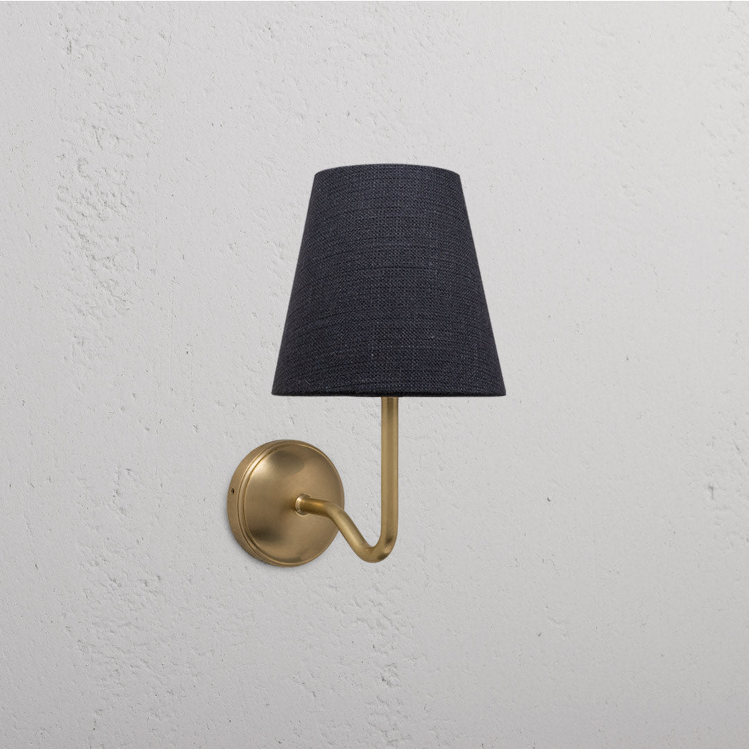 Malvern Medium Wall Light in Basalt Grey and Antique Brass on a textured white wall.