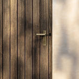 Apsley Long Plate Sprung Door Handle in antique brass on a wooden door with vertical planks.