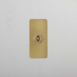 1G Architrave Centre Retractive Toggle Switch in antique brass on a textured white wall, suited for 1G switches & dimmers.