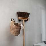 Bronze Hyde Hook securely mounts a broom and basket on a light gray wall, showcasing its stylish design.
